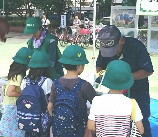 写真：緑色の帽子をかぶった児童らとブースの大人たち