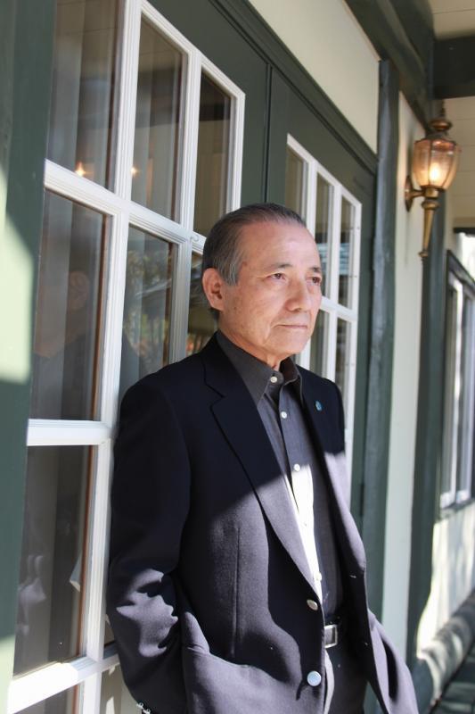 写真：洋風の建物の窓を背に佇む内田康夫氏
