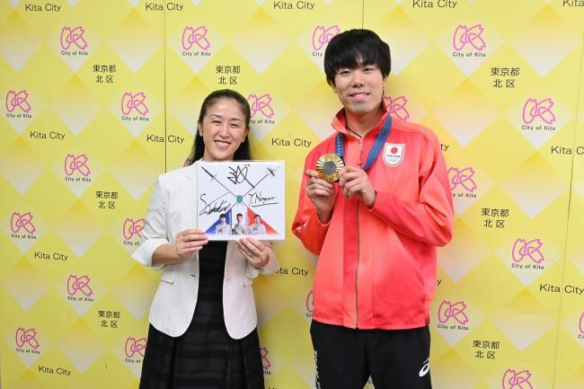 写真：サイン色紙を持って記念撮影する区長と敷根選手