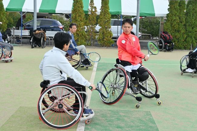 写真：競技用車いすに乗りながらラケットの振り方を教わる参加者