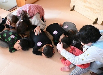 ダンゴムシのポーズで身を守る園児と職員